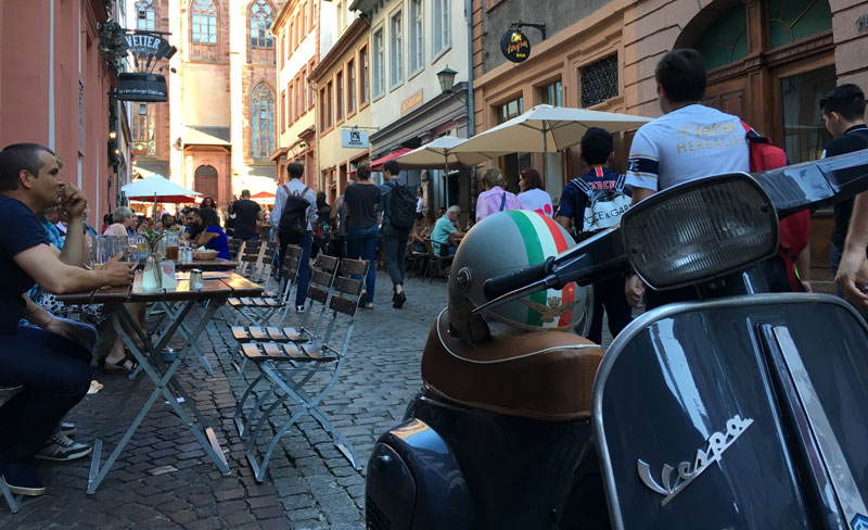 A typical European street scene: outdoor cafes, cobblestones and scooters.